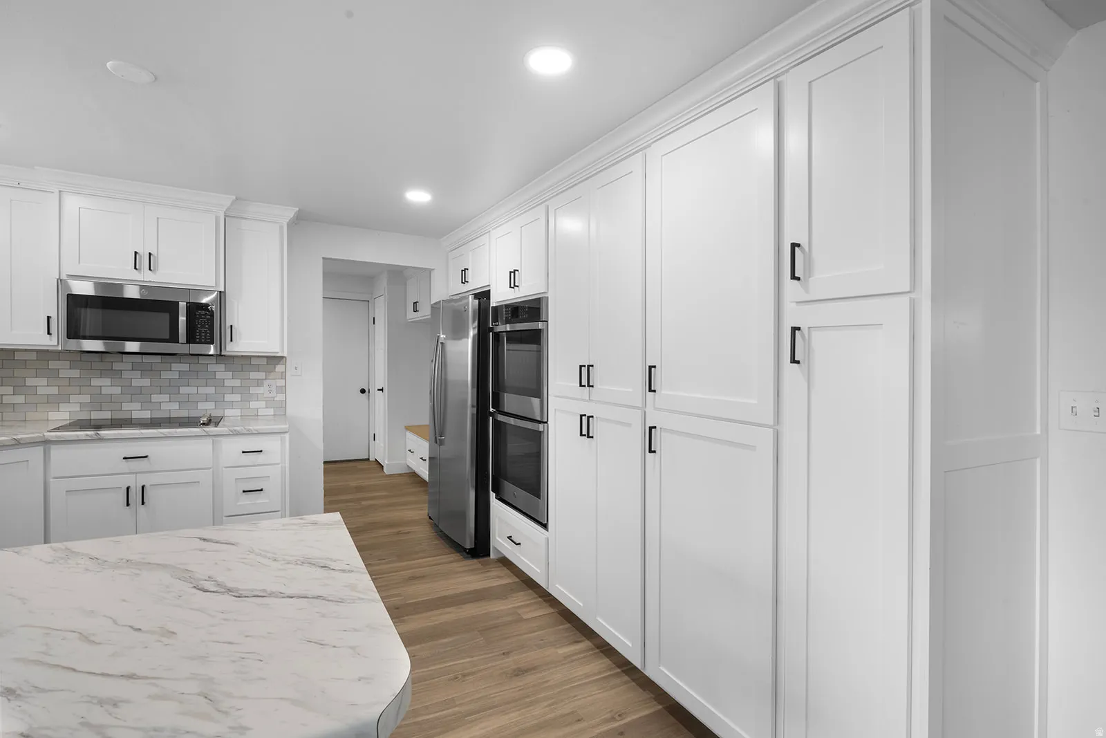 Kitchen with white cabinets, stainless steel appliances, recessed lighting, dark wood-type flooring, and light stone counters