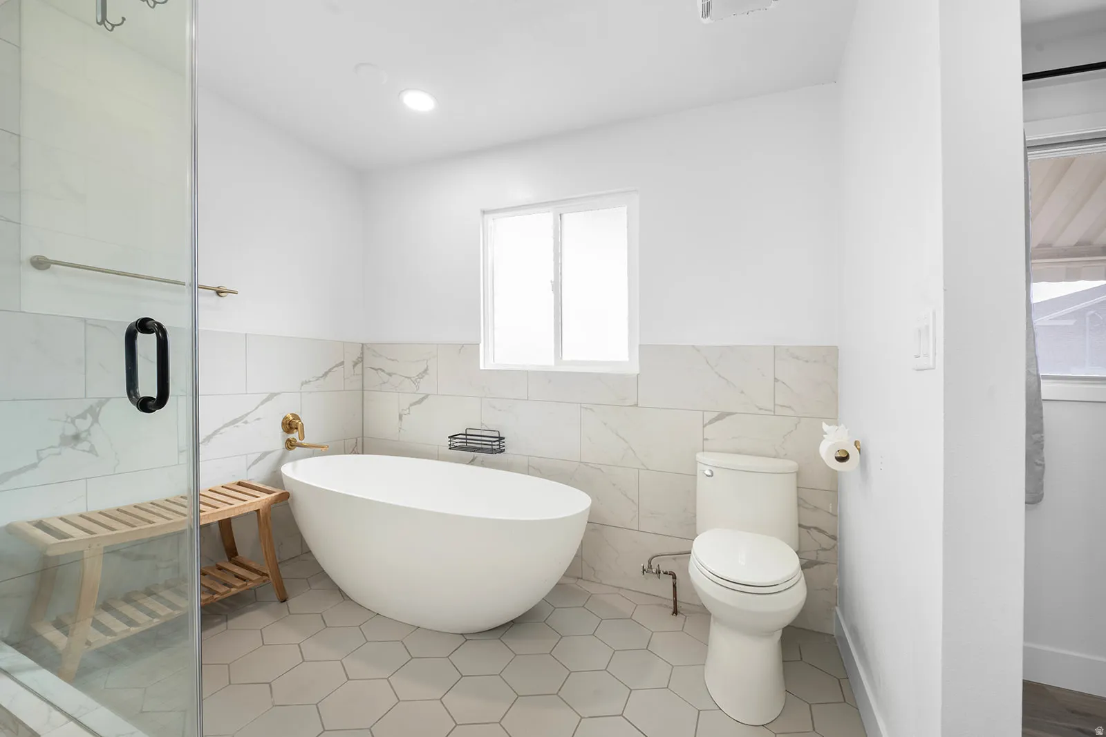 Bathroom featuring a stall shower, tile patterned floors, a freestanding tub, tile walls, and a wainscoted wall