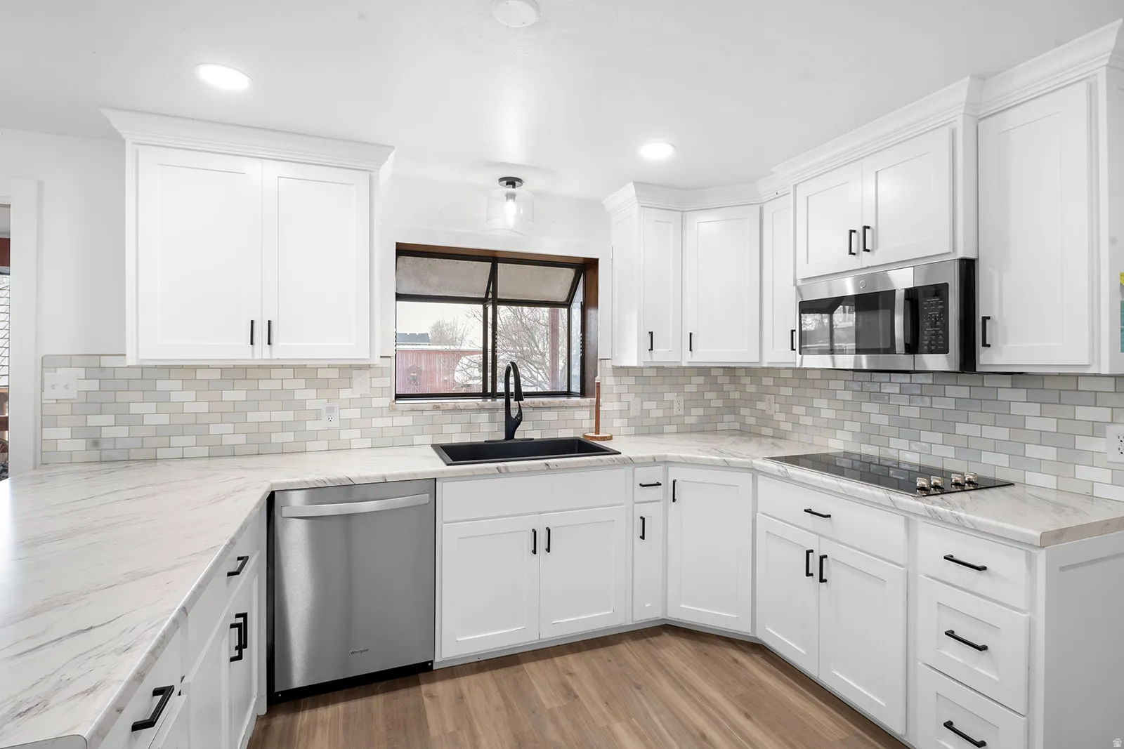 Kitchen with stainless steel appliances, light wood-style floors, white cabinets, light stone counters, and recessed lighting