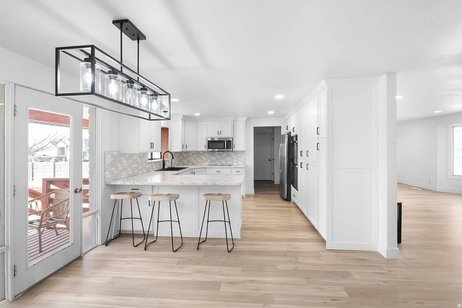 Kitchen featuring a kitchen breakfast bar, a peninsula, light stone counters, light wood-style flooring, and pendant lighting