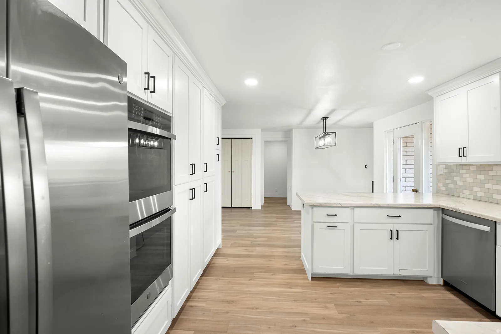 Kitchen featuring stainless steel appliances, white cabinets, a peninsula, light wood finished floors, and decorative backsplash