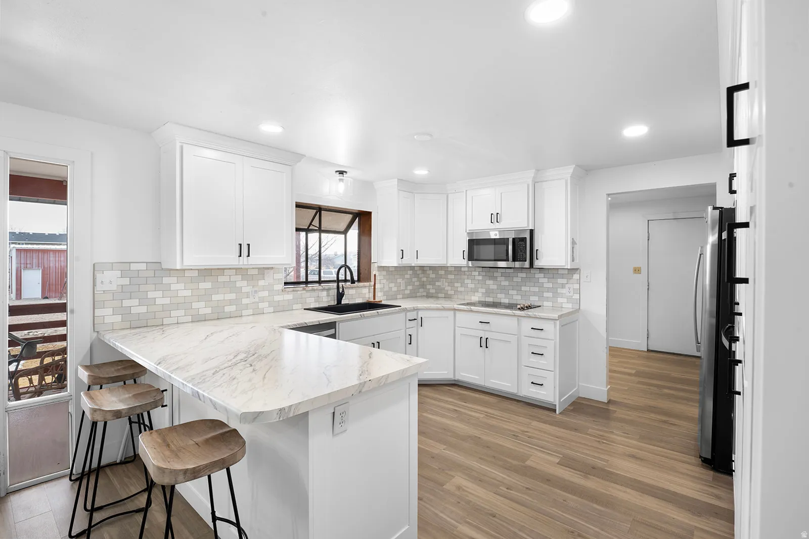 Kitchen featuring a peninsula, a breakfast bar area, white cabinetry, light wood-style flooring, and recessed lighting