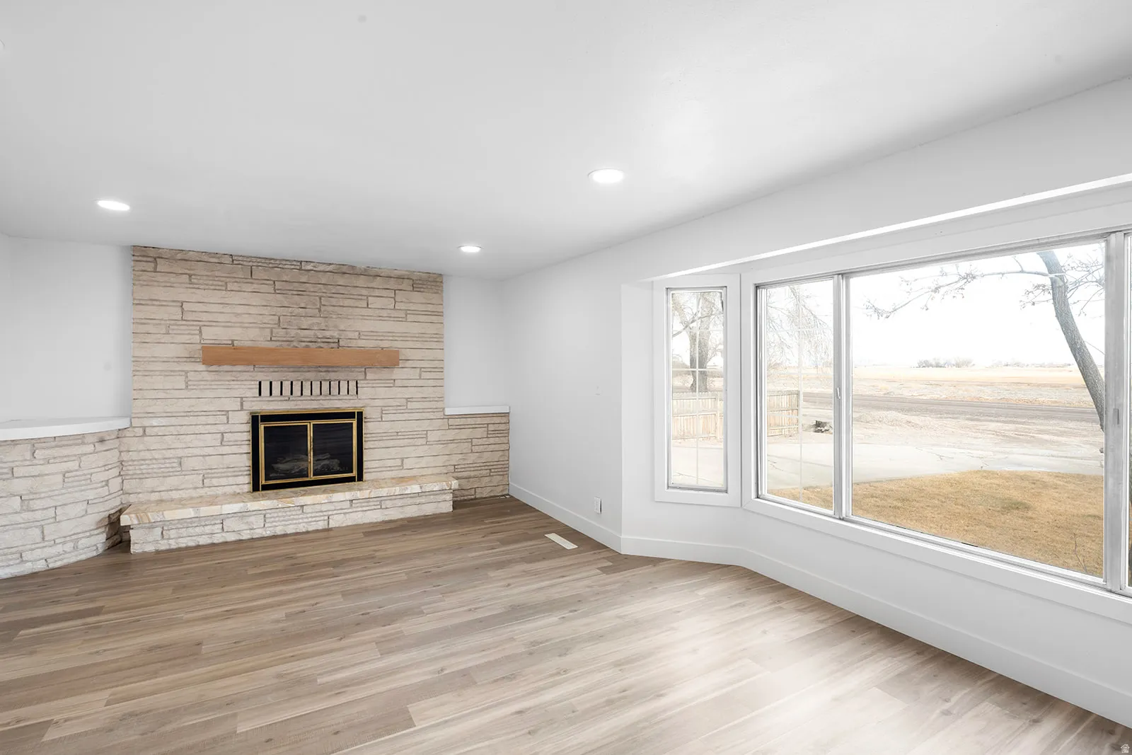 Unfurnished living room featuring light wood-style floors, a stone fireplace, and recessed lighting