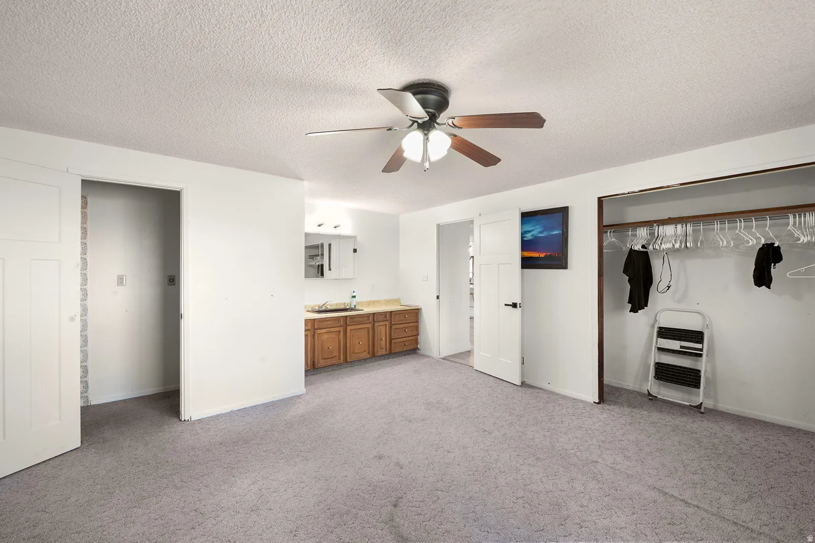 Unfurnished bedroom featuring light colored carpet, heating unit, a closet, a textured ceiling, and ceiling fan