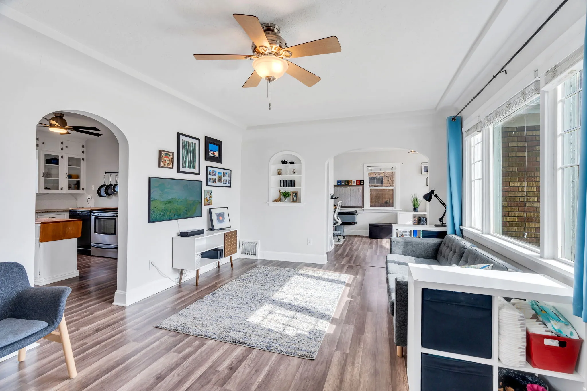 Living room with a ceiling fan, arched walkways, wood finished floors, built in shelves, and ornamental molding