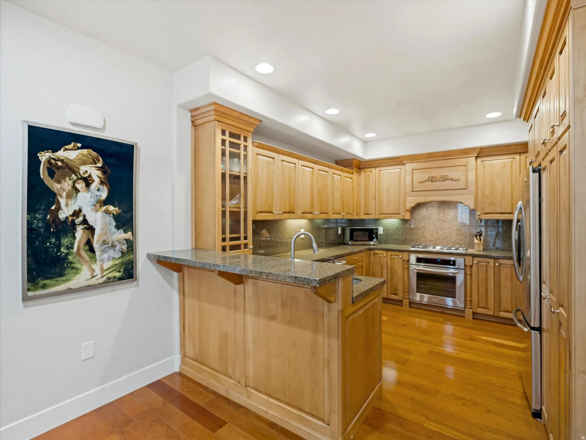 Kitchen with a peninsula, light wood-style floors, backsplash, stainless steel appliances, and a breakfast bar.