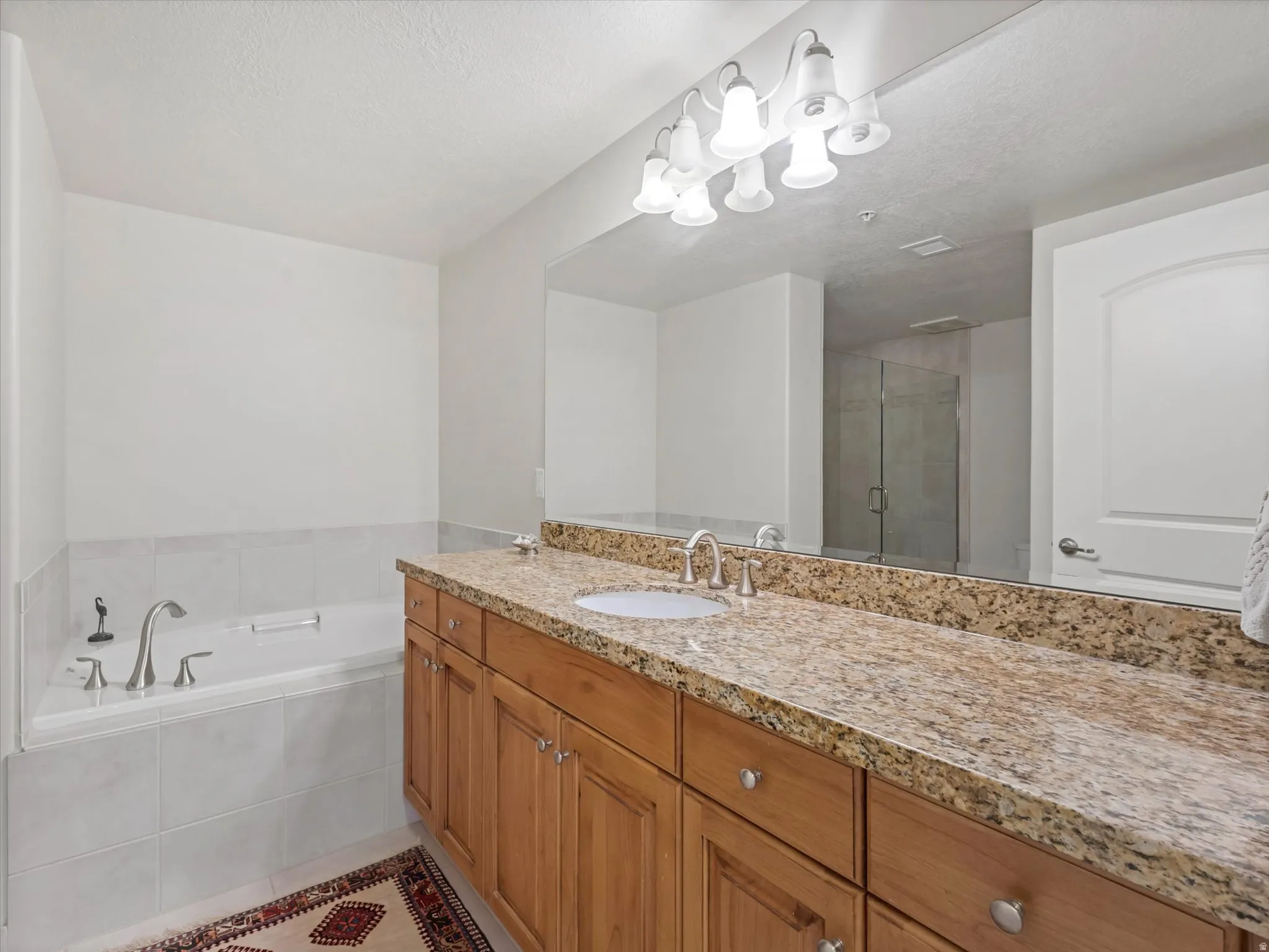 Master bathroom featuring a stall shower, vanity, a garden tub, a textured ceiling, and light tile patterned floors.