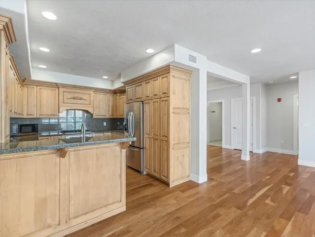 Kitchen with a peninsula, stainless steel appliances, decorative backsplash, light wood-style flooring, and dark stone counters