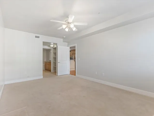 Unfurnished bedroom featuring light carpet, a ceiling fan, ensuite bathroom, and freestanding refrigerator