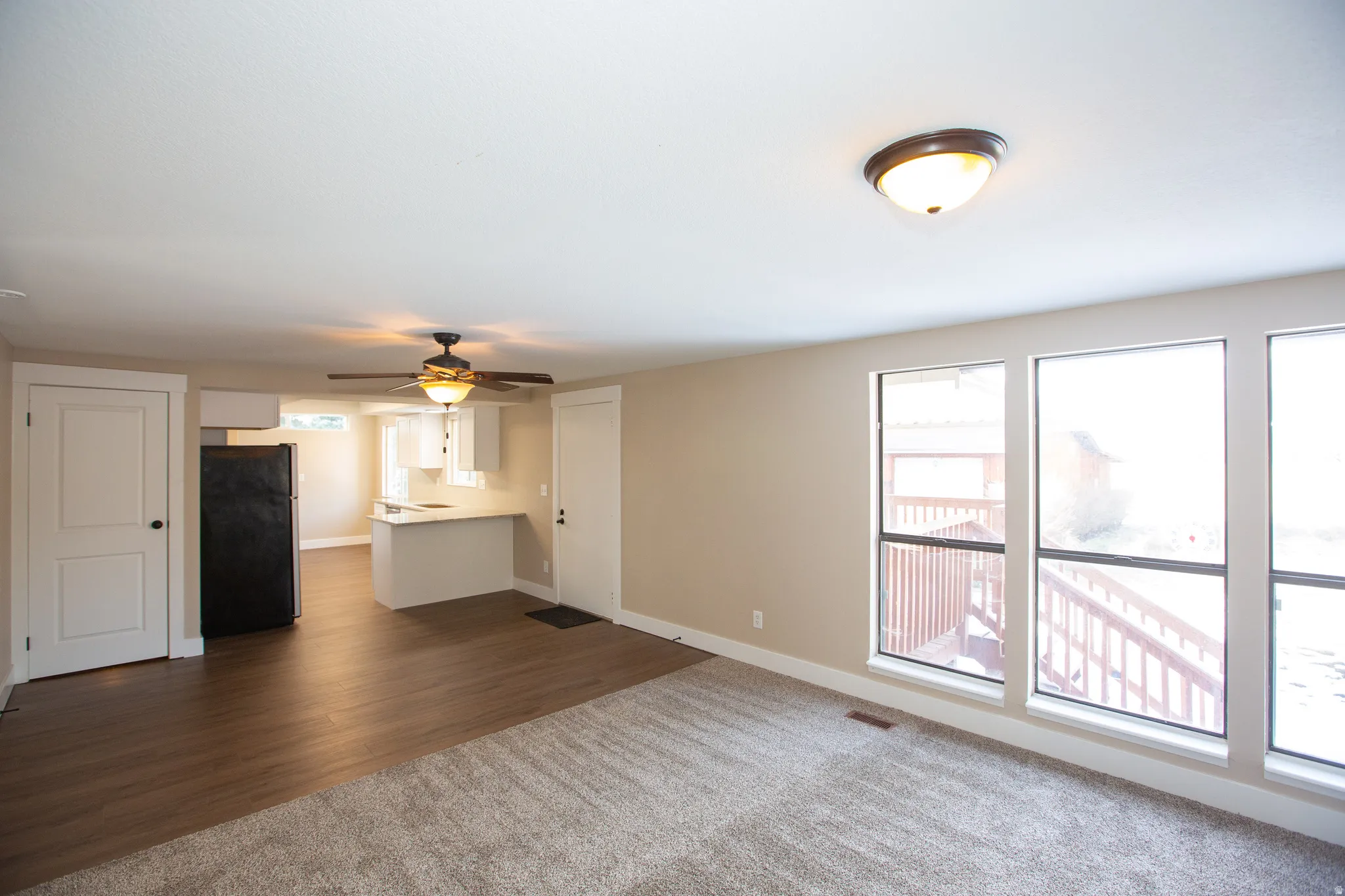 Unfurnished living room with ceiling fan, dark wood finished floors, healthy amount of natural light, and dark colored carpet