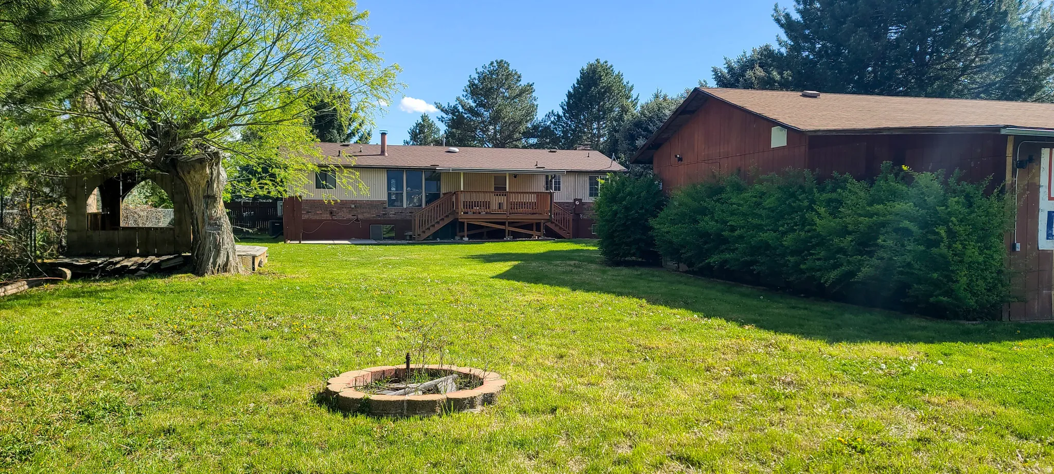 Expansive lawn featuring a brick fire pit, mature trees, and a rear deck with a ramp