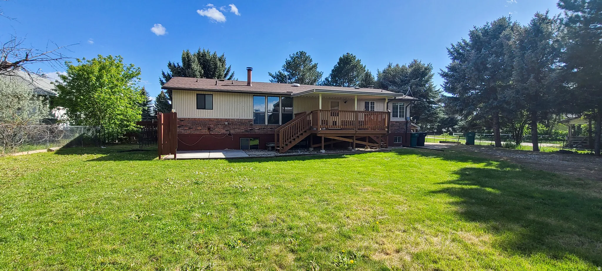 Expansive backyard featuring a manicured lawn, a covered wood deck, and a concrete patio