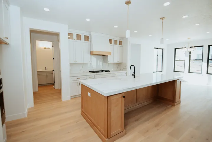 Kitchen with a large island with sink, light stone counters, glass fronted cabinets, backsplash, and hanging light fixtures