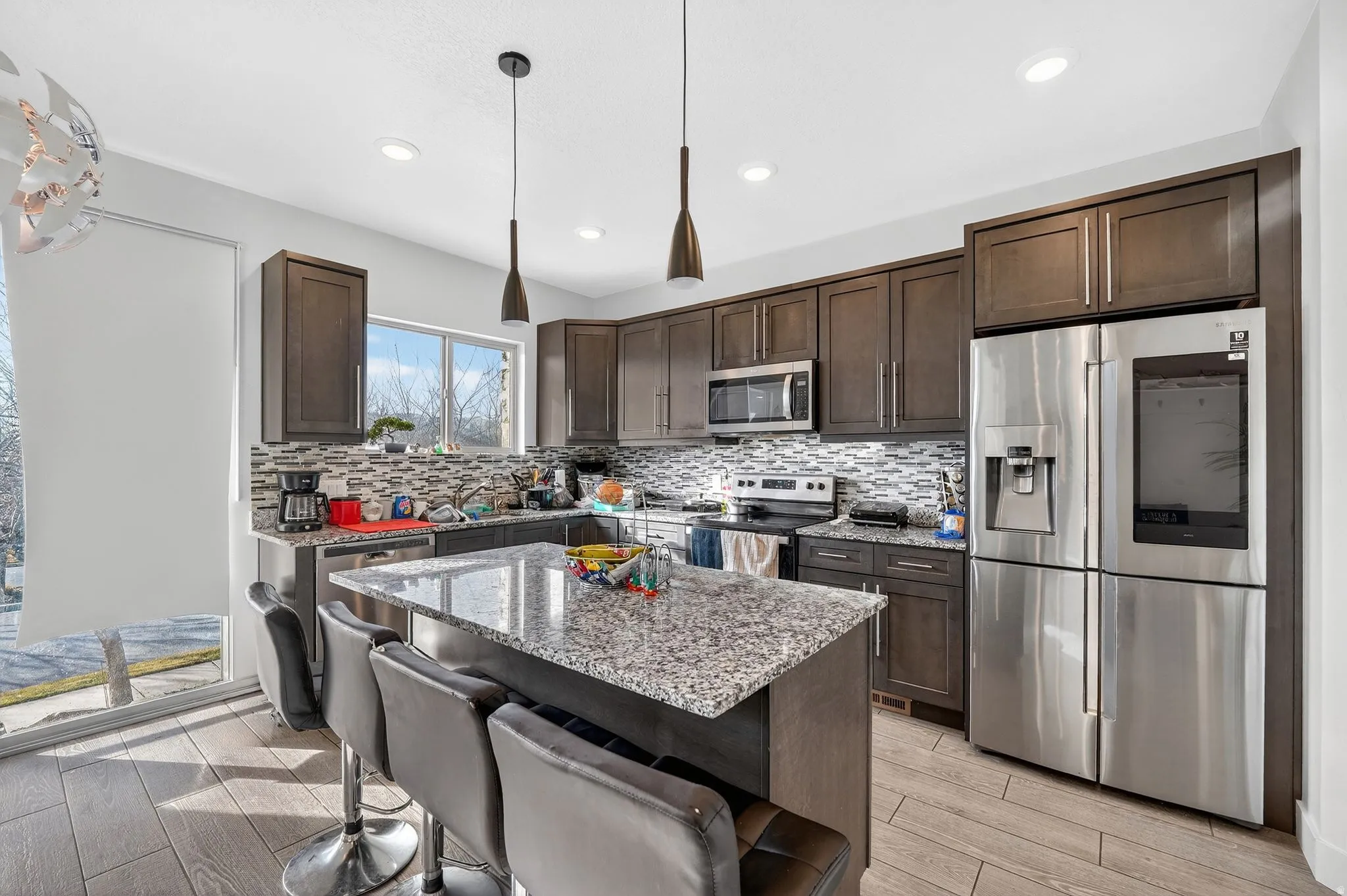 Kitchen featuring stainless steel appliances, a kitchen breakfast bar, dark wood finish cabinets, light stone counters, and wood finish floors