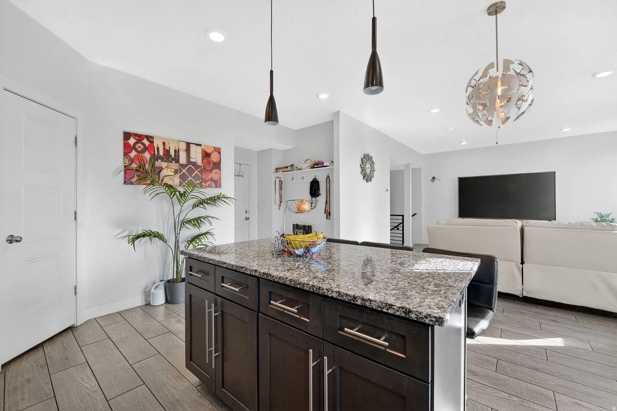 Kitchen with wood finish floors, decorative light fixtures, light stone countertops, a center island, and dark wood finish cabinets