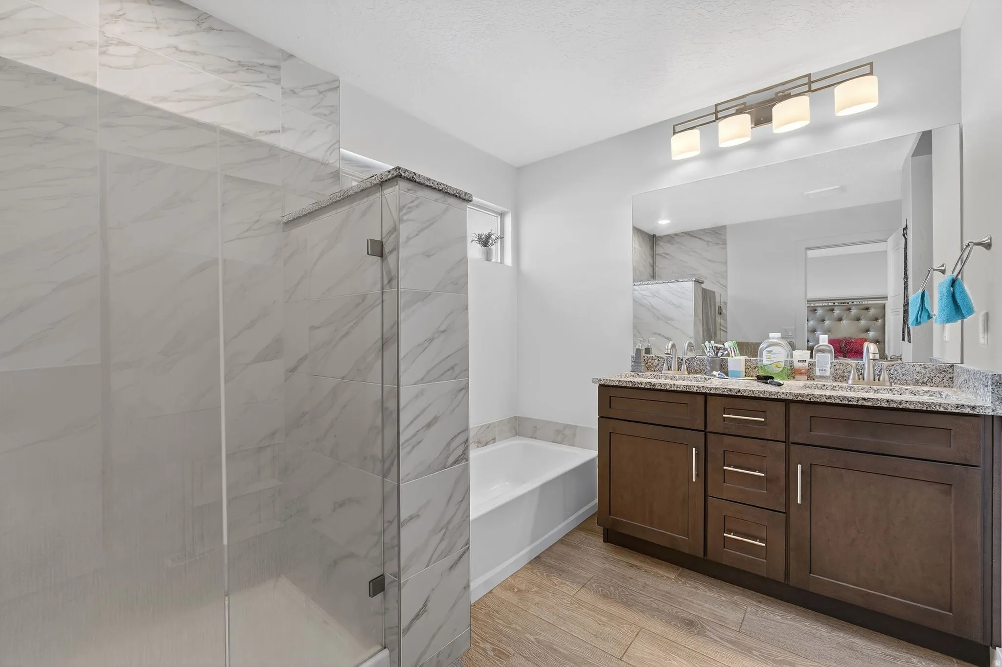 Full bathroom with double vanity, a bath, light wood-type flooring, and a marble finish shower