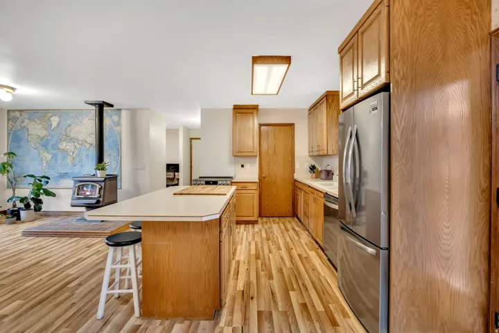 Kitchen featuring light countertops, stainless steel appliances, a breakfast bar area, light wood-style floors, and a wood stove