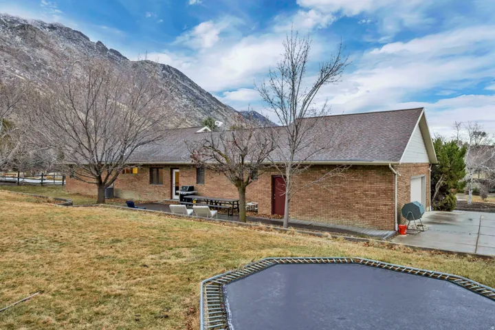 Back of house featuring a trampoline, a patio area, a yard, a mountain view, and brick siding