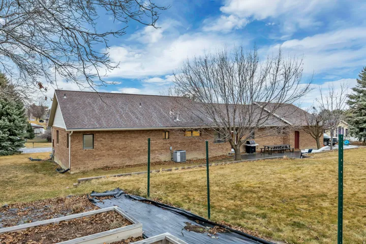 View of side of property featuring brick siding, a shingled roof, a yard, a patio, and a vegetable garden