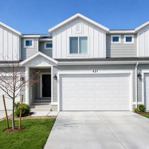View of front of home with board and batten siding, an attached garage, driveway, and a front yard