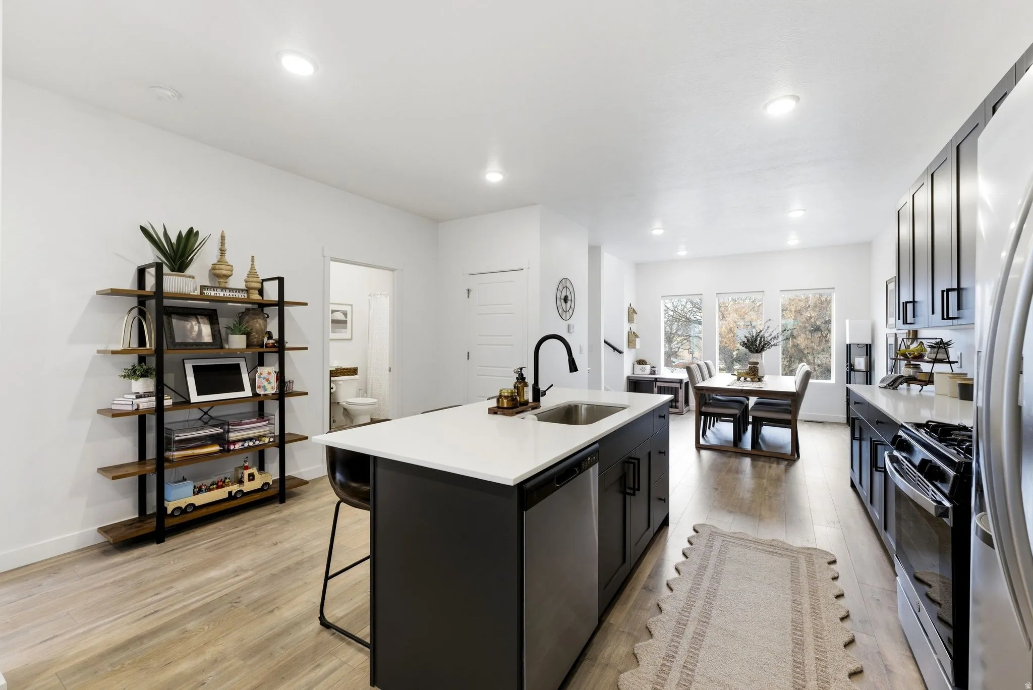 Kitchen featuring dark cabinets, a center island with sink, stainless steel appliances, light wood-style floors, and a kitchen bar