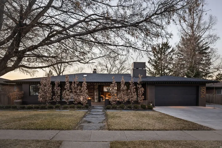 View of front of house featuring a chimney, concrete driveway, a garage, a lawn, and a porch