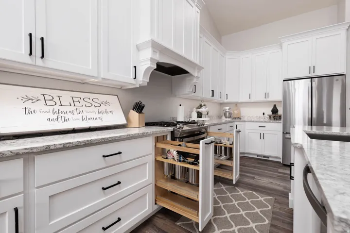 Kitchen with white cabinetry, light stone counters, freestanding refrigerator, and dark wood-style flooring