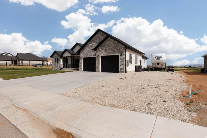 View of front of house with stone siding, driveway, an attached garage, a porch, and a front yard