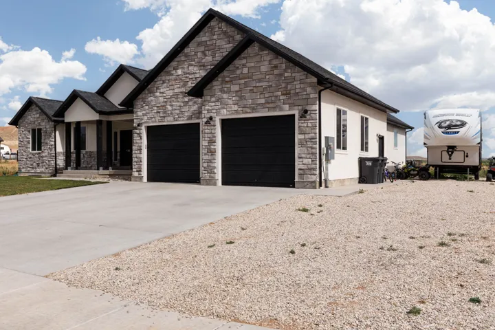 View of front of home with driveway, stone siding, an attached garage, stucco siding, and covered porch