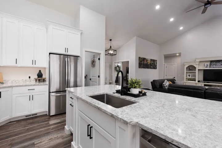 Kitchen featuring freestanding refrigerator, white cabinets, open floor plan, a ceiling fan, and light stone countertops