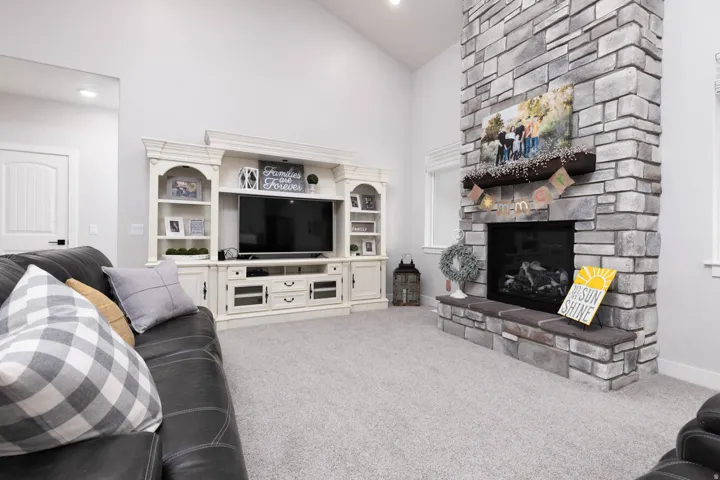 Living area featuring light carpet, lofted ceiling, and a stone fireplace