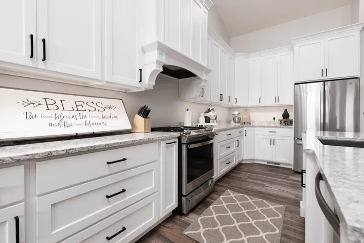 Kitchen featuring stainless steel appliances, white cabinetry, light stone counters, and dark wood-style floors