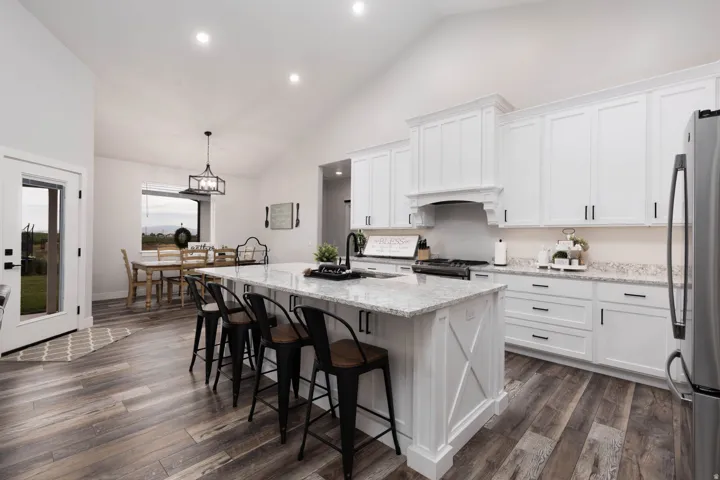 Kitchen with light stone counters, a center island with sink, white cabinets, stainless steel appliances, and vaulted ceiling