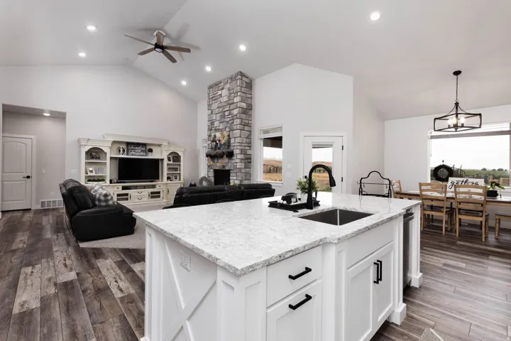 Kitchen featuring vaulted ceiling, light stone countertops, a fireplace, ceiling fan, and white cabinetry