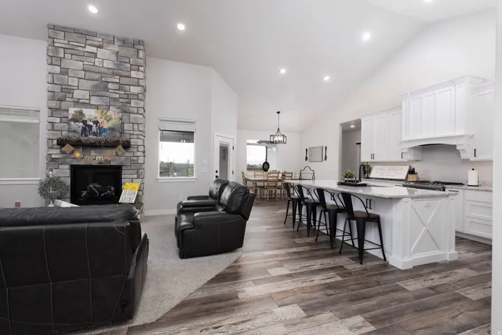 Living area with a stone fireplace, dark wood-type flooring, vaulted ceiling, and recessed lighting
