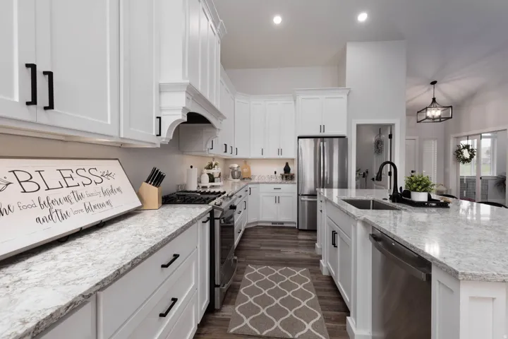 Kitchen with stainless steel appliances, white cabinets, light stone counters, and an island with sink