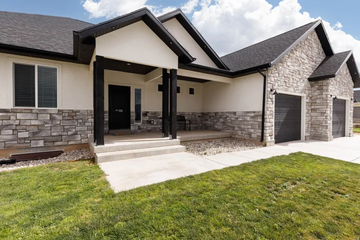 View of front of house with stone siding, a porch, stucco siding, an attached garage, and a front lawn
