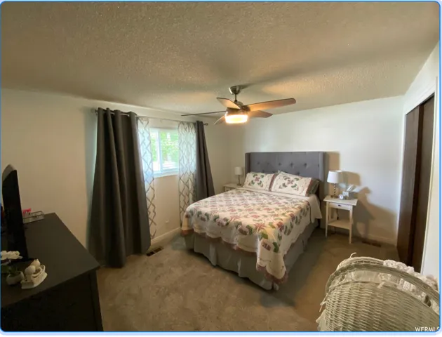 Bedroom featuring a textured ceiling, light colored carpet, ceiling fan, and a closet