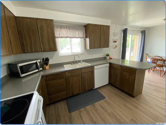 Kitchen with a peninsula, white appliances, light wood finished floors, and healthy amount of natural light