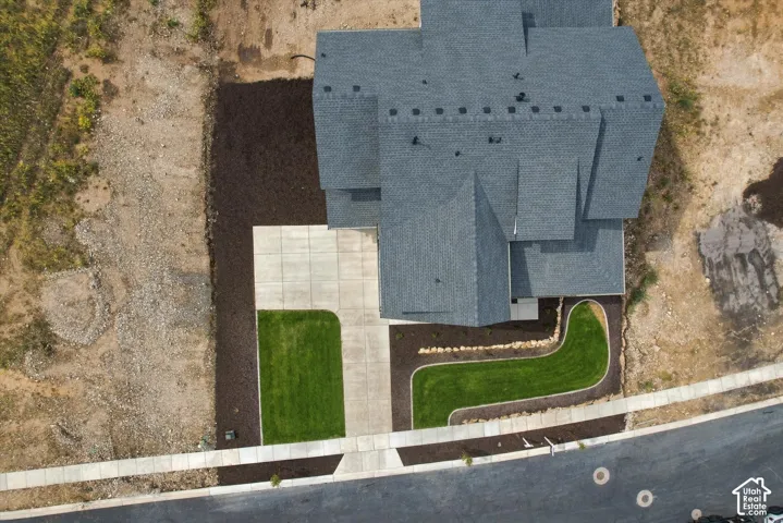 Aerial perspective featuring a multi-gabled asphalt shingle roof, concrete driveway, and established turf landscaping with curved stone edging