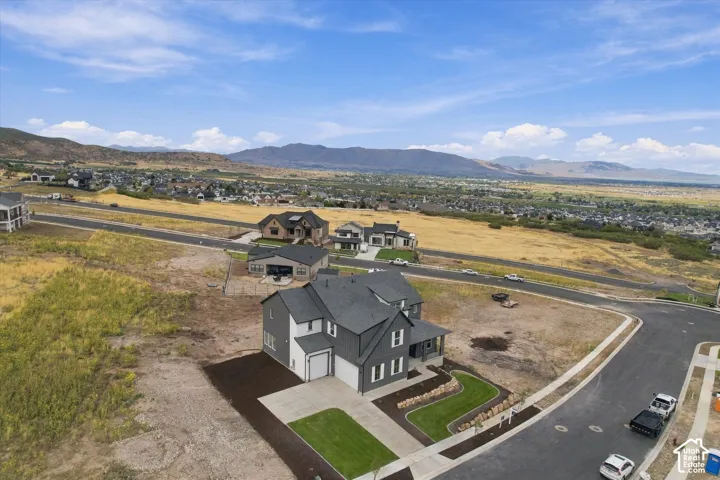 Multi-level residence featuring a dark gray and white exterior, steep-pitched roofline, concrete driveway, attached garage, and surrounding mountain range scenery