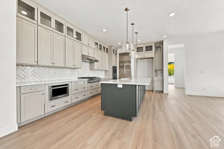 Kitchen featuring floor-to-ceiling cabinetry, a central island with a quartz countertop, herringbone tile backsplash, wood-finish flooring, and pendant lighting