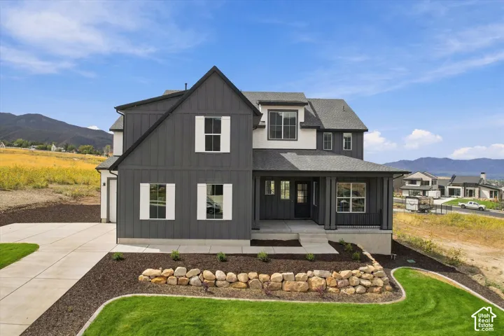 Two-story exterior with vertical siding and contrasting trim, covered front porch, stone retaining wall, concrete driveway, and mountain backdrop
