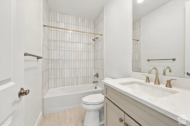 Bathroom featuring a vanity with quartz countertop, under-mount sink, brass-finish fixtures, vertical-stacked wall tile, and a porcelain-finish soaking tub