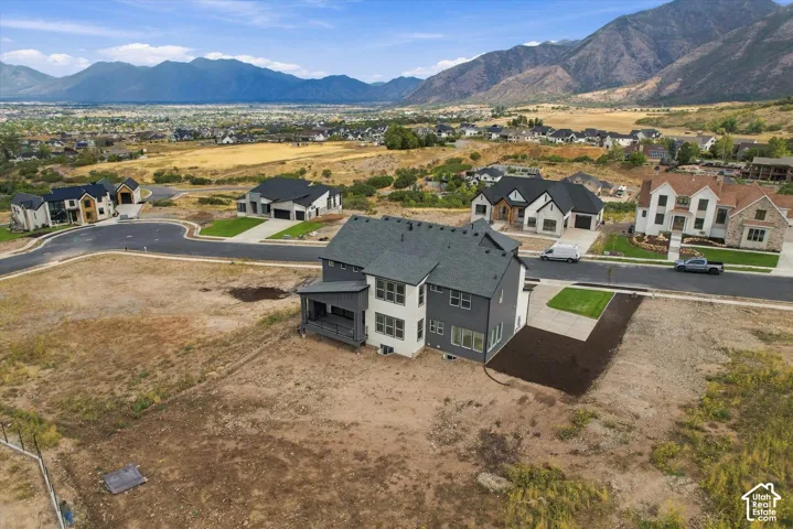 Multi-story residential property featuring a dark shingle roof, neutral exterior siding, a covered rear porch, and a paved driveway, set against a backdrop of mountain scenery