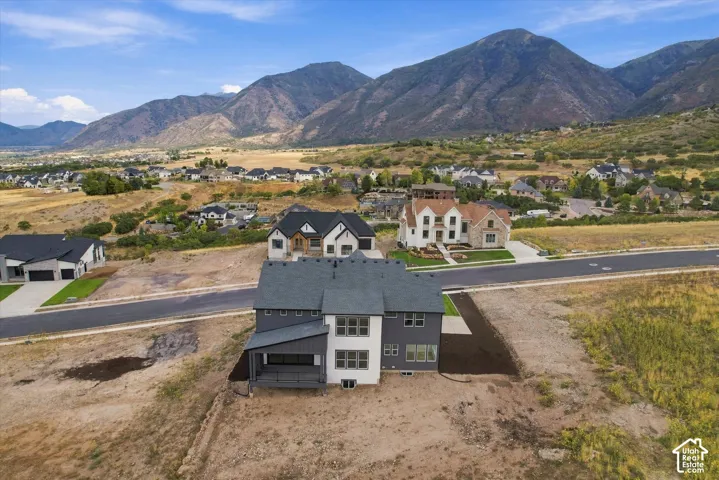 Aerial perspective of a multi-story residence featuring a dark-toned shingle roof, a covered patio with metal roofing, multi-pane windows, and a mountain backdrop