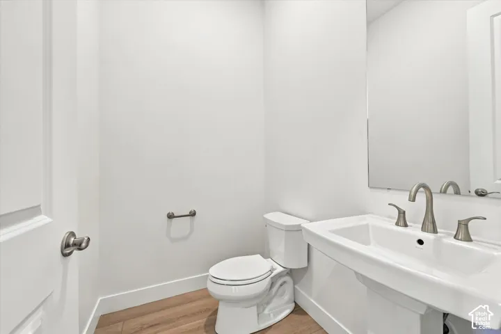 Pedestal sink featuring a brushed-nickel faucet, oversized wall-mounted mirror, white ceramic toilet, and wood-finish flooring