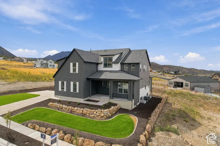 Two-story residence featuring vertical siding, a covered front porch, stacked stone retaining walls, and a concrete driveway