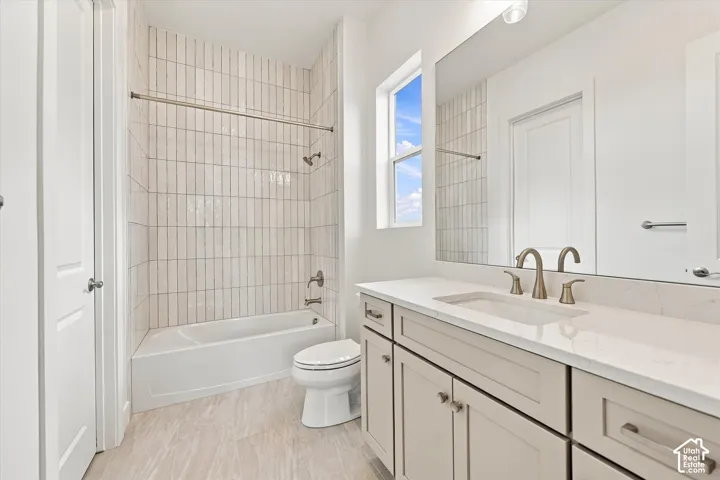 Bathroom featuring a vanity with neutral-toned cabinetry, light-colored stone-look countertop, vertical tile shower surround, and large wall-mounted mirror