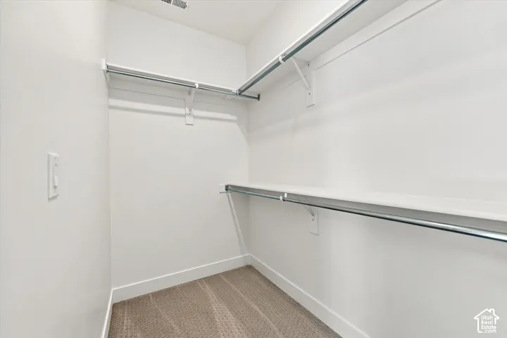 Walk-in storage space featuring neutral carpeting and tiered built-in shelving with integrated metal clothing rods
